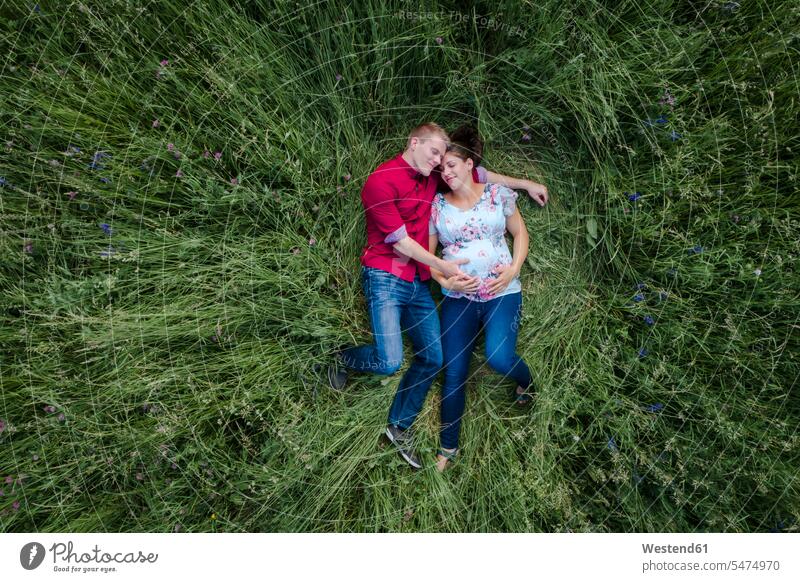Pregnant woman and man holding baby belly, lying on meadow touch Secure happy Emotions Feeling Feelings Sentiment Sentiments loving closeness propinquity