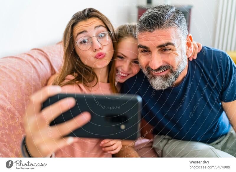 Happy father with two daughters taking selfie on couch at home T- Shirt t-shirts tee-shirt couches settee settees sofa sofas telecommunication phones telephone