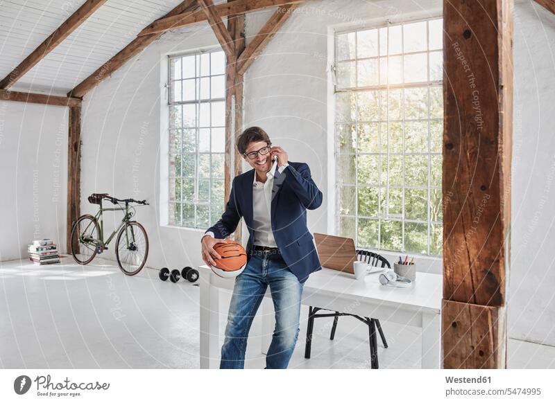 Smiling businessman with basketball on cell phone in penthouse Penthouse Businessman Business man Businessmen Business men on the phone call telephoning