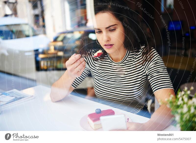 Young woman using cell phone and eating cake at an cafe in the city mobile phone mobiles mobile phones Cellphone cell phones town cities towns pies cakes