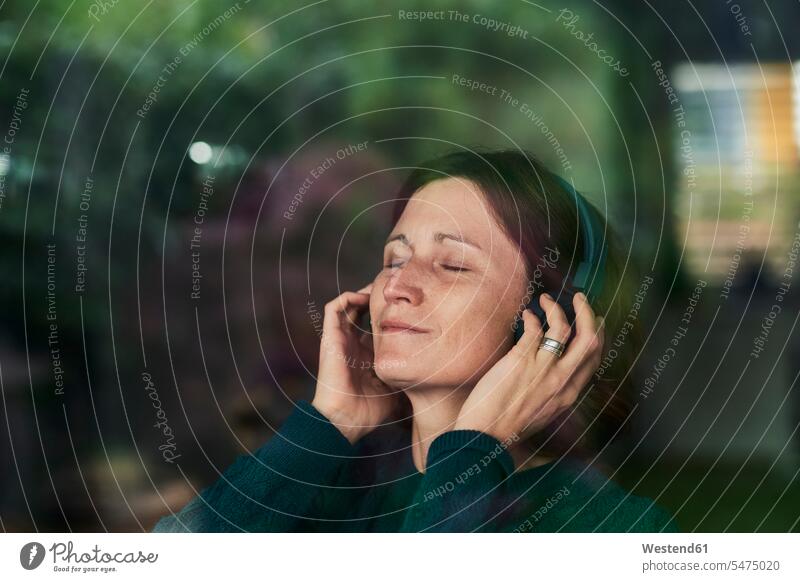 Close-up of woman with eyes closed enjoying music listening through headphones at home color image colour image outdoors location shots outdoor shot