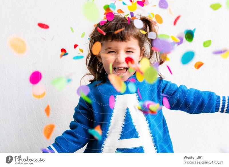Happy little girl blowing the confetti at a party in front of a white wall jumper sweater Sweaters fall tumble tumbling celebrate partying smile Ardor Ardour