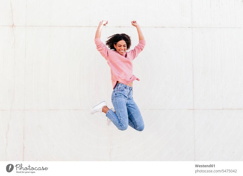Happy young woman jumping in the air against light background Leaping happiness happy females women jump in the air jumps Adults grown-ups grownups adult people