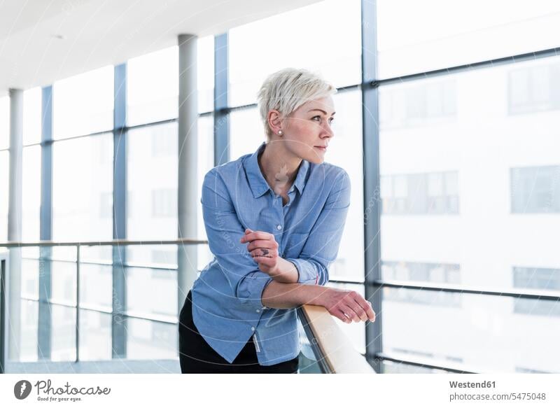 Woman in office building leaning on railing office buildings Railing Railings rested on woman females women built structure built structures Adults grown-ups