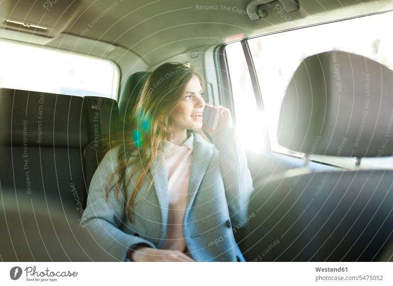 Young businesswoman on the phone sitting on backseat of a car looking out of window businesswomen business woman business women windows automobile Auto cars