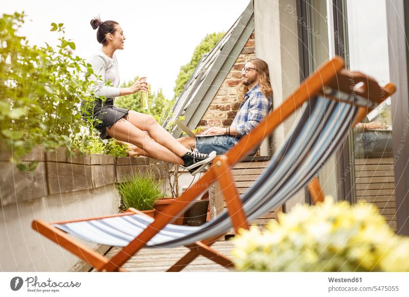Young couple sitting on their balcony in summer, talking and using laptop summer time summery summertime Plant Plants Surfing the Net balconies leisure