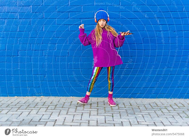 Girl wearing blue cap and oversized pink pullover listening music with headphones in front of blue wall Spain Leggings Smartphone iPhone Smartphones Hand Raised