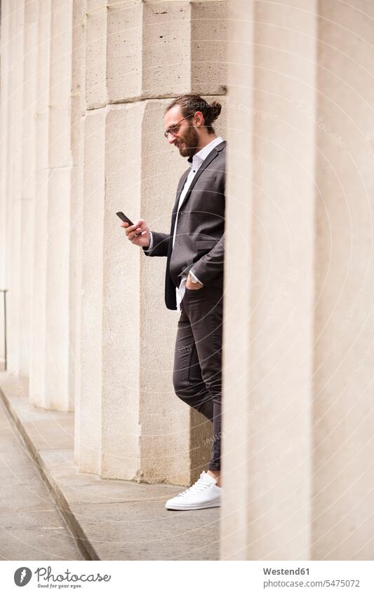 Young businessman standing among columns of Stock Exchange looking at cell phone, New York City, USA business life business world business person businesspeople