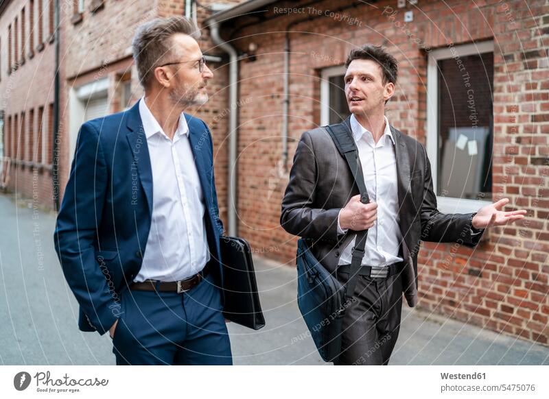 Two businessmen walking and talking at an old brick building brick buildings going discussing discussion executive Executives manager Business Meeting