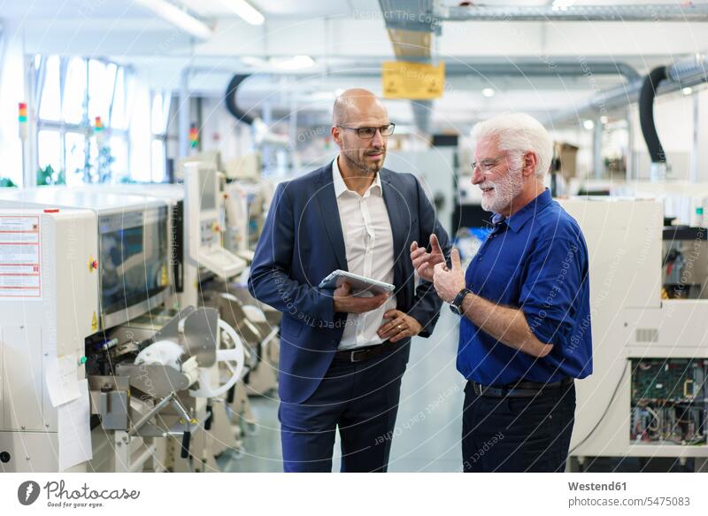 Businessman holding digital tablet while looking at senior manager discussing at illuminated factory color image colour image indoors indoor shot indoor shots