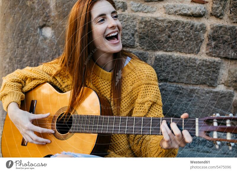 Red-haired woman playing the guitar in the city Singer musician female musician musicians females women Passion passionate guitars singing singers Adults