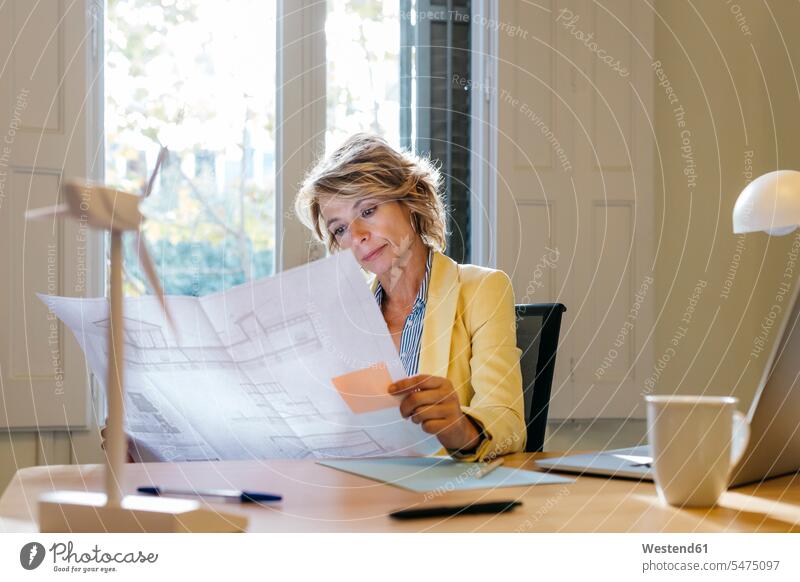 Female engineer analyzing blueprint while sitting in office color image colour image indoors indoor shot indoor shots interior interior view Interiors day