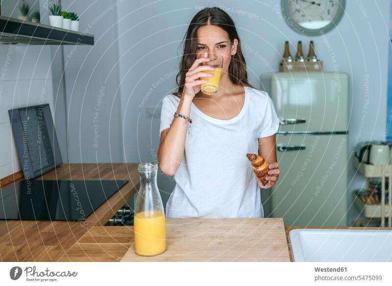 Young woman having breakfast with juice and croissant in the kitchen human human being human beings humans person persons caucasian appearance