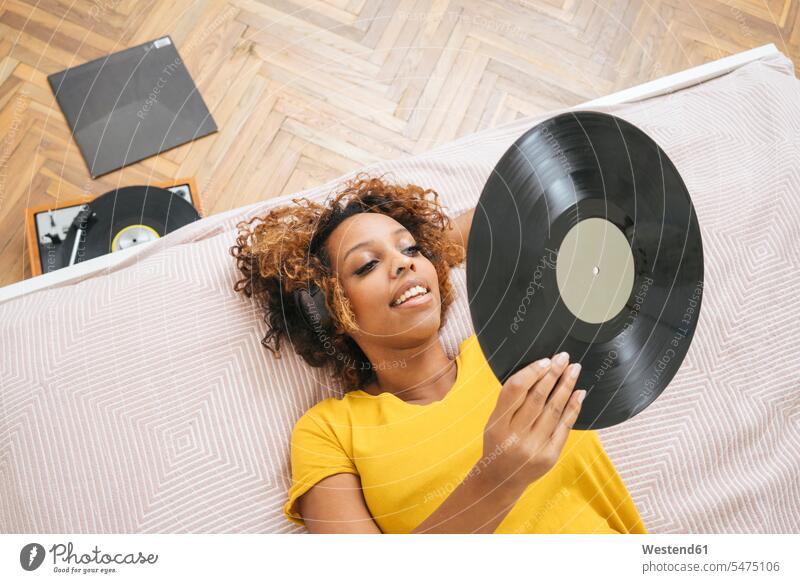 Young woman lying on bed listening to music with headphones and record player human human being human beings humans person persons celibate celibates singles