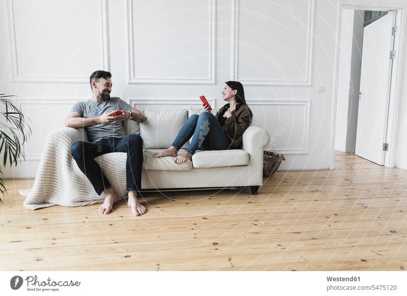 Couple sitting at home on couch, using their smartphones caucasian caucasian ethnicity caucasian appearance european Seated dark hair dark-haired living room