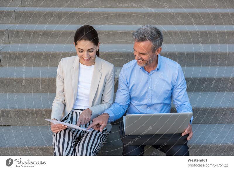 Two business people sitting side by side on stairs working together businesspeople Seated stairway At Work paralell Juxtaposed in paralell business world