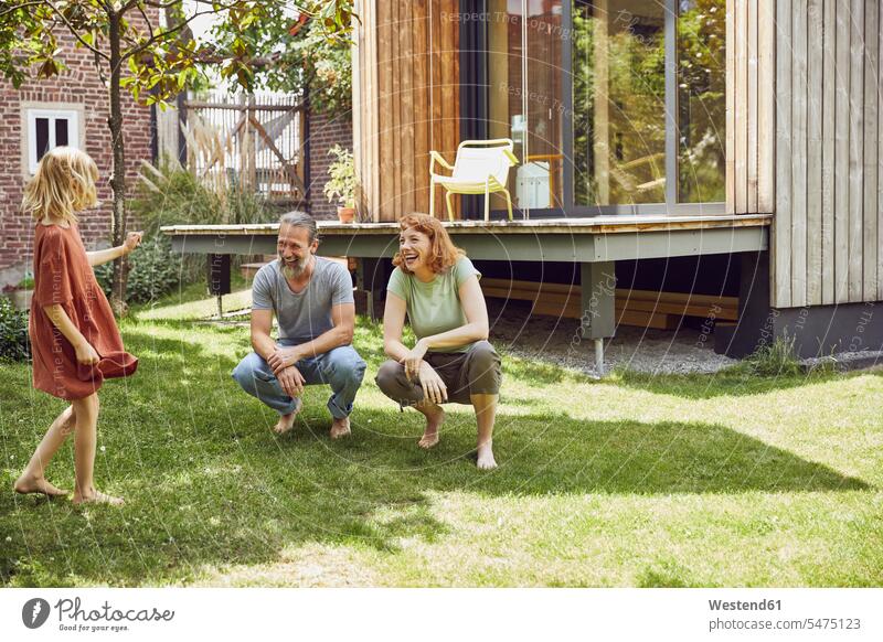 Cheerful parents looking at daughter while crouching on grassy land in yard color image colour image Germany leisure activity leisure activities free time