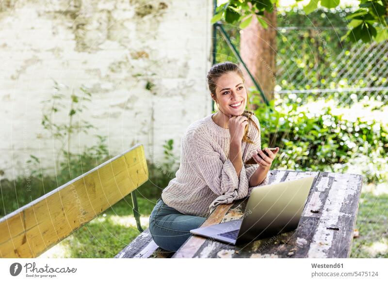 Happy daydreaming woman sitting in the garden with laptop and cell phone day dreaming Daydreams Day Dream gardens domestic garden Laptop Computers laptops