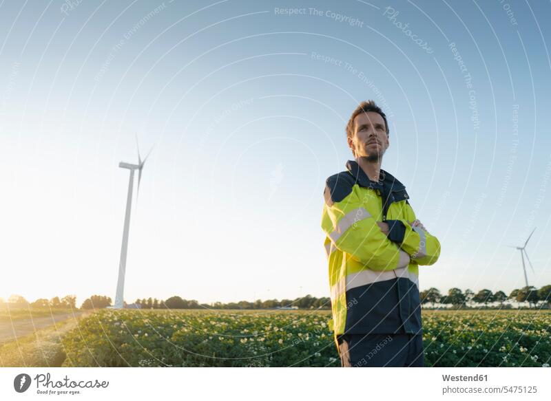 Engineer standing in a field at a wind turbine engineer engineers wind turbines Field Fields farmland engineering engineering science technology technologies
