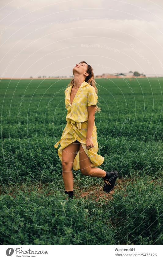 Young woman walking in a green field smiling smile going dress dresses summer summer time summery summertime yellow females women running Adults grown-ups