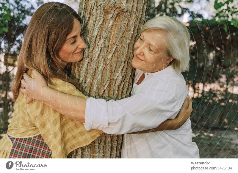 Mother and daughter looking at each other while embracing tree trunk in yard color image colour image Spain leisure activity leisure activities free time