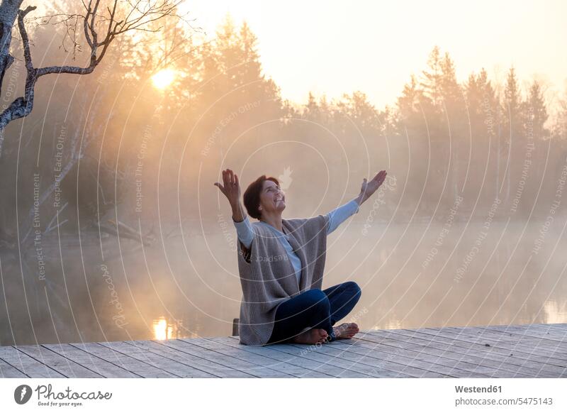 Adult woman meditating on lakeshore jetty at foggy sunrise outdoors location shots outdoor shot outdoor shots Lakeshore Lake Shore lakeside water's edge