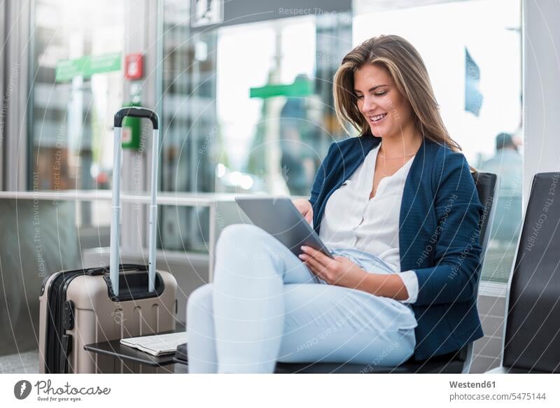 Young businesswoman with luggage sitting at waiting area using tablet digitizer Tablet Computer Tablet PC Tablet Computers iPad Digital Tablet digital tablets