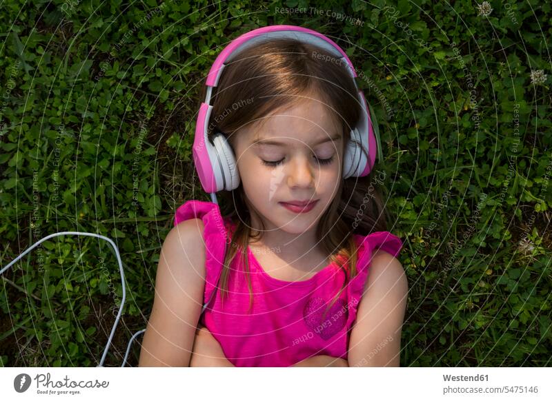 Portrait of girl lying on a meadow listening music with pink headphones hearing laying down lie lying down meadows portrait portraits headset magenta females