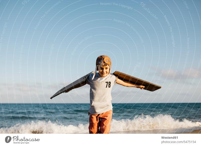 Boy wearing aviator's cap and cardboard wings at beach color image colour image outdoors location shots outdoor shot outdoor shots day daylight shot