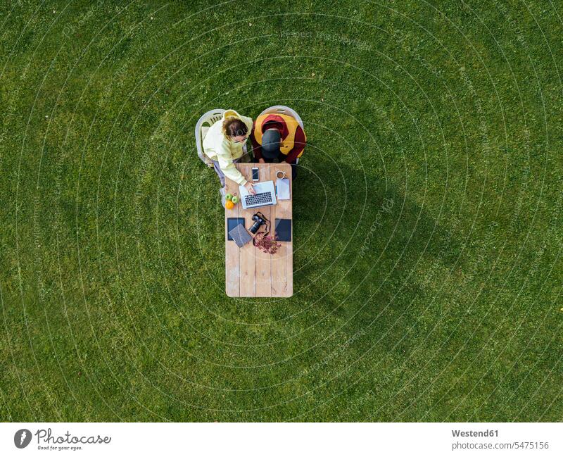 Aerial view of man and woman working together on laptop at coffee table set on green lawn outdoors location shots outdoor shot outdoor shots day daylight shot