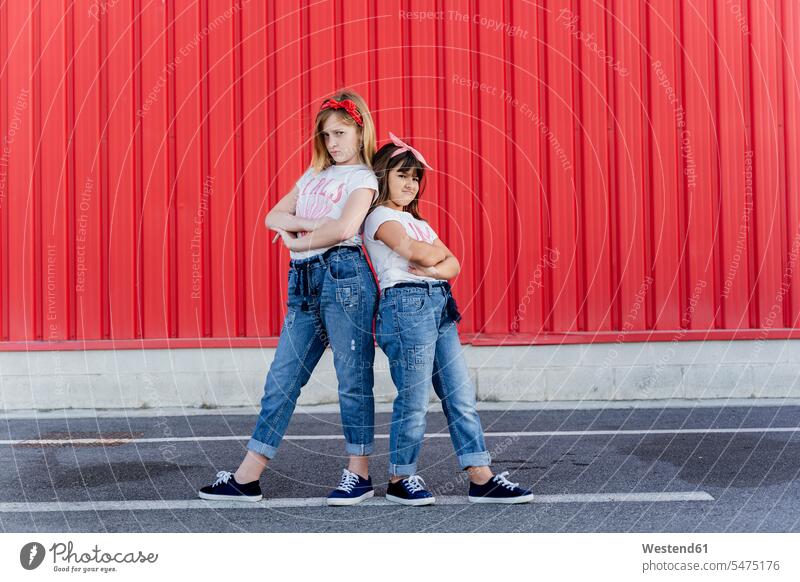 Two sisters standing in front of a red wall friends mate female friend pants Trouser Denim Jeans T- Shirt t-shirts tee-shirt delight enjoyment Pleasant pleasure