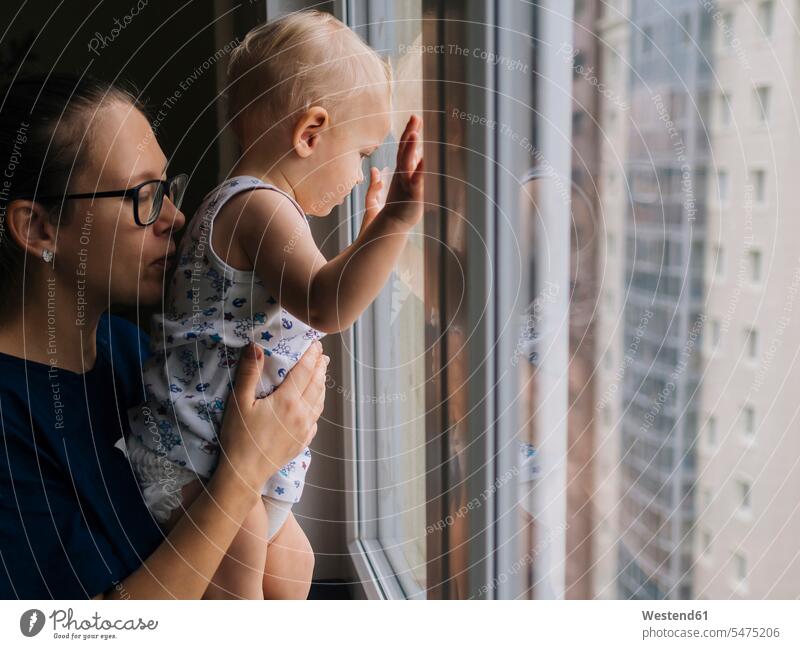 Mother holding baby boy looking through window at home color image colour image indoors indoor shot indoor shots interior interior view Interiors day