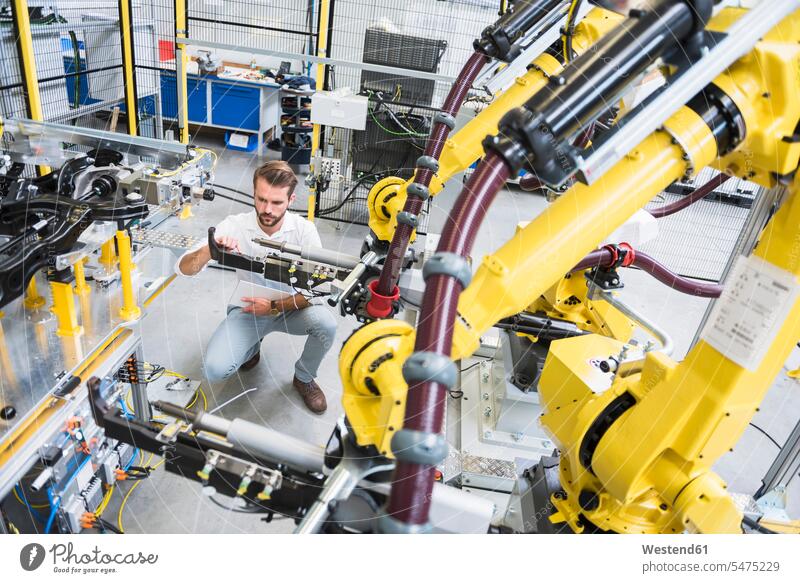 Full length of young engineer crouching while examining computer-aided machinery in automated industry color image colour image Germany indoors indoor shot