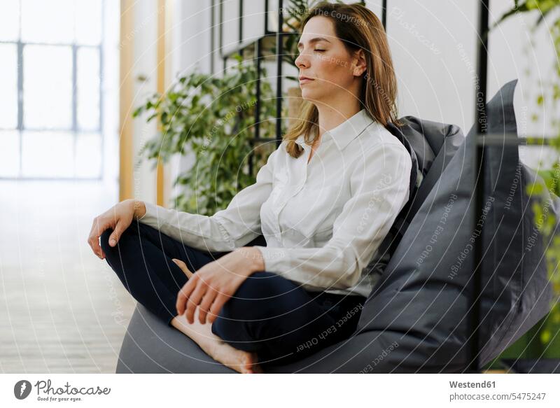 Woman practicing yoga while sitting on bean bag at office color image colour image indoors indoor shot indoor shots interior interior view Interiors day