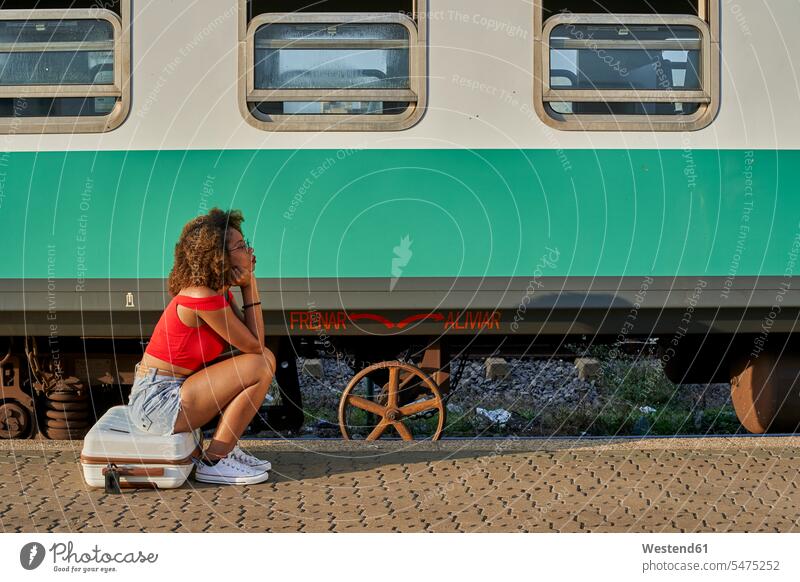 Woman with suitcase sitting at the train station red curly curly hair curls curled waiting passenger train sexy Travel side view sideview View From Side leisure