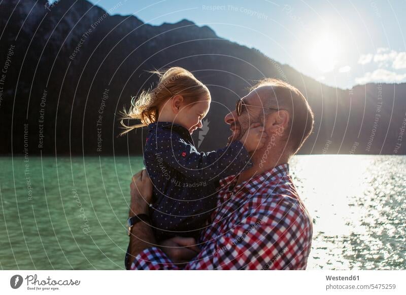 Father carrying daughter against mountain and lake at Achensee, Tyrol State, Austria color image colour image outdoors location shots outdoor shot outdoor shots