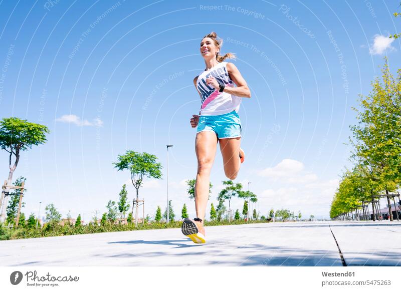 Mid adult woman jogging on street against blue sky color image colour image Spain outdoors location shots outdoor shot outdoor shots day daylight shot