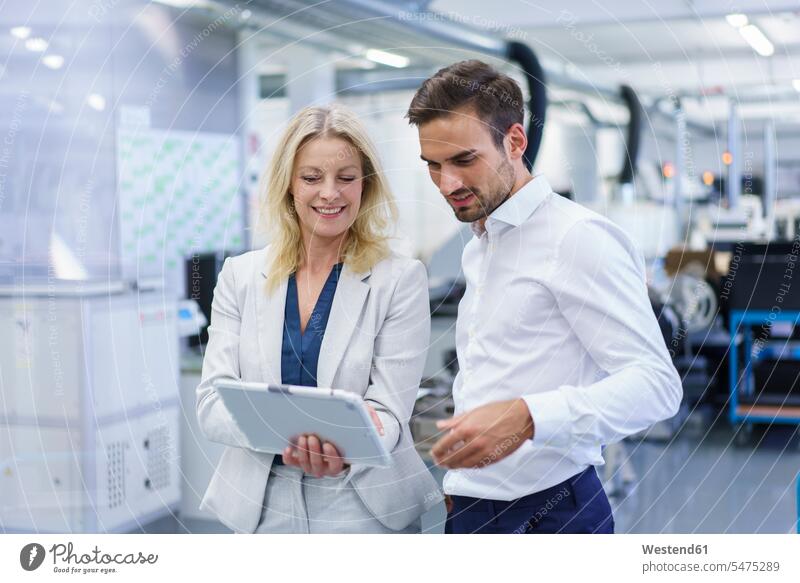 Smiling blond businesswoman discussing over digital tablet with male colleague at factory color image colour image indoors indoor shot indoor shots interior