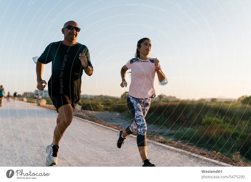 Woman running with senior sportsman on road during sunset color image colour image outdoors location shots outdoor shot outdoor shots sunsets sundown atmosphere