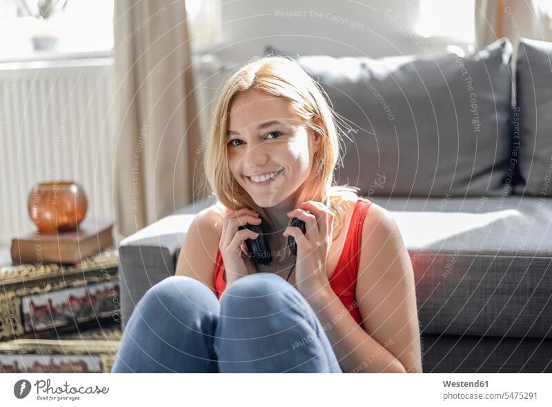 Portrait of happy young woman sitting on the floor at home listening music with headphones human human being human beings humans person persons celibate