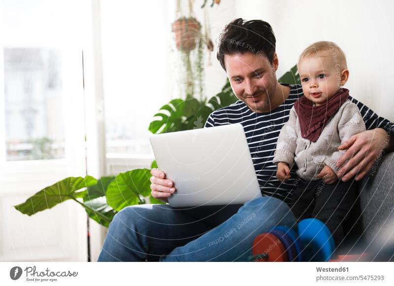 father sitting on couch with his little daughter, using laptop using a laptop Using Laptops pa fathers daddy dads papa daughters Seated Laptop Computers laptops