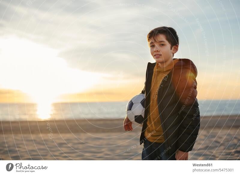 Portrait of boy holding football on the beach at sunset beaches soccer ball soccer balls footballs portrait portraits sunsets sundown boys males atmosphere