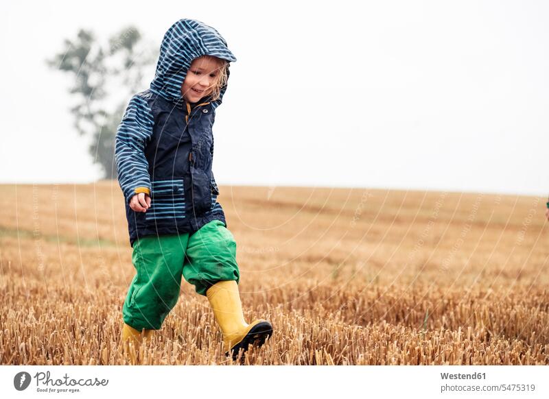 Happy little girl walking on stubble field at rainy day hoods shoes boots Gumboot Gumboots Rubber Boot rubber boots wellies Wellington Boots wellingtons Ardor