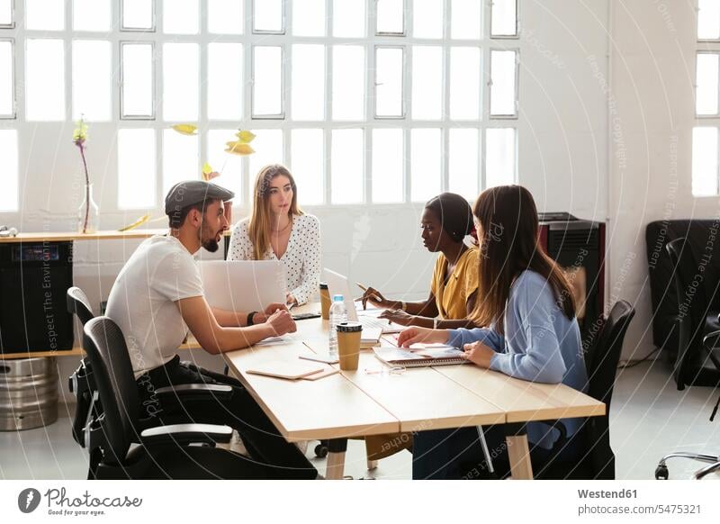 Colleagues working together at desk in office desks business people businesspeople colleagues At Work offices office room office rooms Table Tables