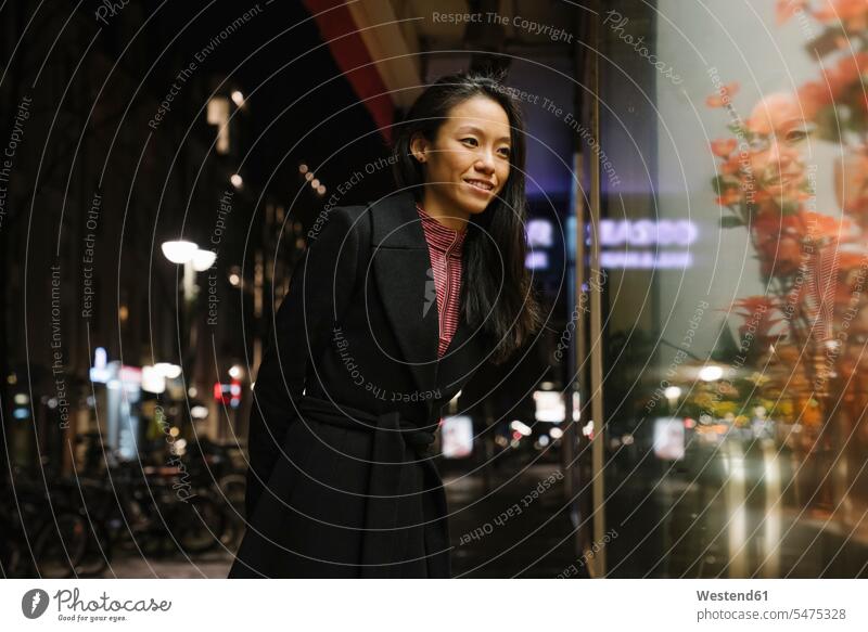 Smiling young woman looking in shop window at night, Frankfurt, Germany business life business world business person businesspeople business woman