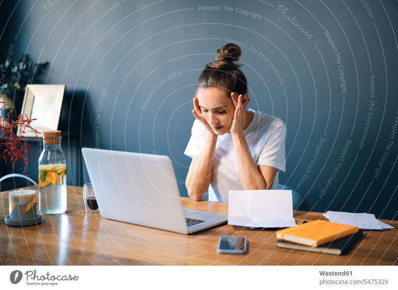 Female entrepreneur with head in hands sitting at desk against wall color image colour image casual clothing casual wear leisure wear casual clothes