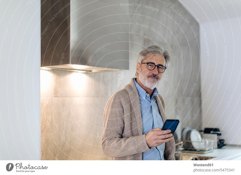 Portrait of mature man with cell phone in kitchen at home human human being human beings humans person persons celibate celibates singles solitary people