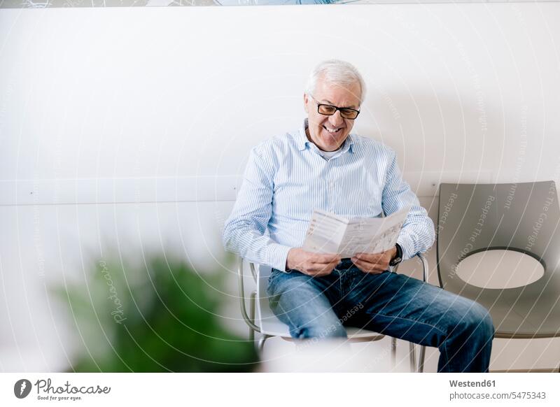 Senior man sitting in waiting room of medical practice, reading leaflet human human being human beings humans person persons caucasian appearance