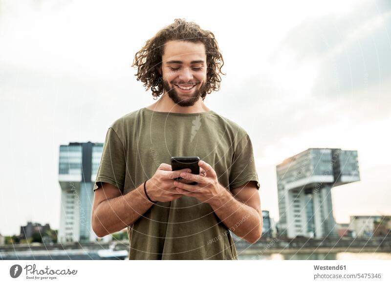 Germany, Cologne, smiling young man looking at cell phone smile eyeing mobile phone mobiles mobile phones Cellphone cell phones view seeing viewing telephones