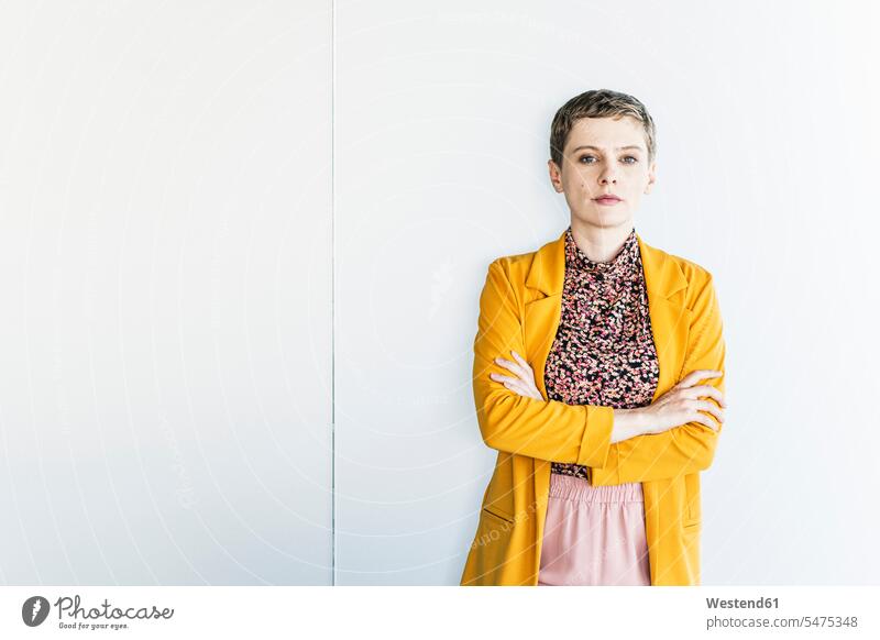 Confident businesswoman wearing yellow blazer standing against white wall in office color image colour image Germany indoors indoor shot indoor shots interior